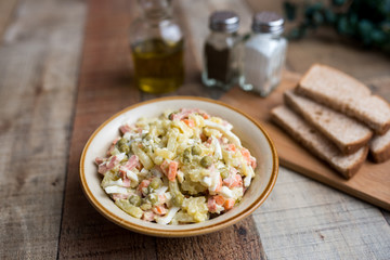 Bowl of traditional Russian salad called Olivie, Russian New Year or Christmas salad on wooden background. Salad from cooked vegetables. Potato salad. 