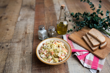 Bowl of traditional Russian salad called Olivie, Russian New Year or Christmas salad on wooden background. Salad from cooked vegetables. Potato salad. 