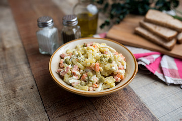 Bowl of traditional Russian salad called Olivie, Russian New Year or Christmas salad on wooden background. Salad from cooked vegetables. Potato salad. 