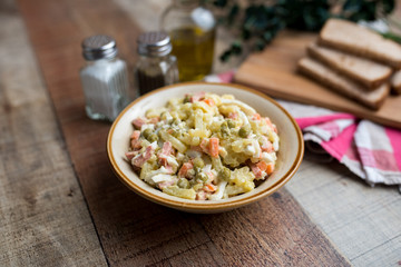 Bowl of traditional Russian salad called Olivie, Russian New Year or Christmas salad on wooden background. Salad from cooked vegetables. Potato salad. 