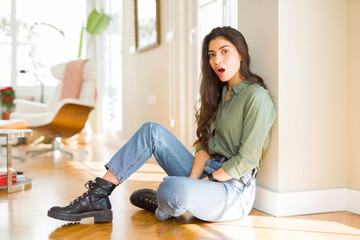 Young beautiful woman sitting on the floor at home afraid and shocked with surprise expression, fear and excited face.