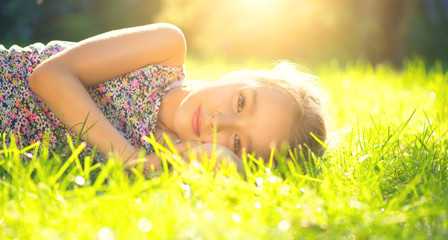 Portrait of a smiling little girl lying on green grass. Cute six years old child enjoying nature in...