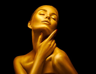 Model girl with shiny golden professional makeup over black. Beauty sexy woman with golden skin....