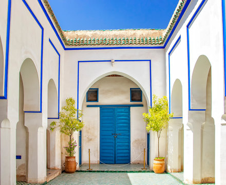 Courtyard at El Bahia Palace, Marrakech, Morocco. there are white walls and columns with blue signs and blue doors.