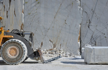A Loader with fork and a block of white marble in a marble quarry, open mining