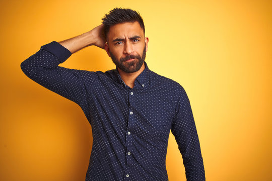 Young handsome indian businessman wearing shirt over isolated yellow background confuse and wonder about question. Uncertain with doubt, thinking with hand on head. Pensive concept.