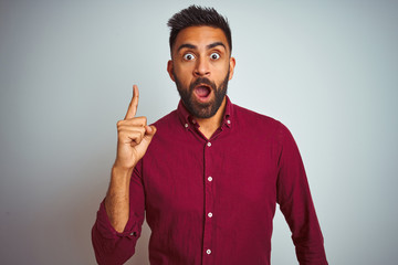 Young indian man wearing red elegant shirt standing over isolated grey background pointing finger up with successful idea. Exited and happy. Number one.