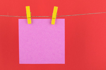 paper sheets of a notebook for notes and reminders of pink color, fastened with decorative yellow clothespins hang on a rope on a red background