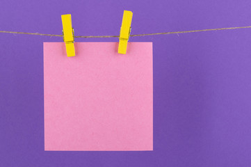paper sheets of a notebook for notes and reminders of pink color fastened with decorative yellow clothespins hang on a rope on a purple background
