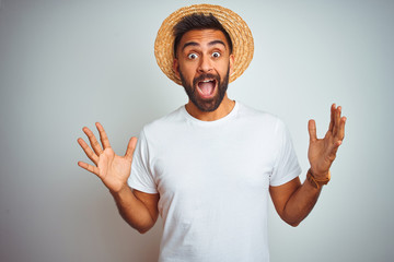 Young indian man on holiday wearing summer hat standing over isolated white background celebrating...