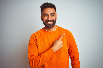 Young indian man wearing orange sweater over isolated white background cheerful with a smile of face pointing with hand and finger up to the side with happy and natural expression on face