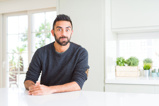 Handsome hispanic man wearing casual sweater at home puffing cheeks with funny face. Mouth inflated with air, crazy expression.