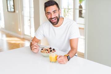 Handsome man smiling eating healthy breakfast and drinking orange juice in the morning