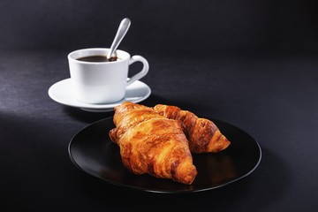 cup of black coffee and croissant on black