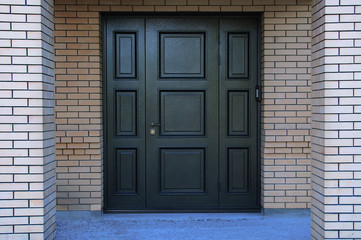 Black metal entrance door in a brick house.