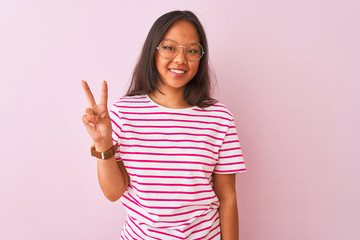 Young chinese woman wearing striped t-shirt and glasses over isolated pink background showing and pointing up with fingers number two while smiling confident and happy.