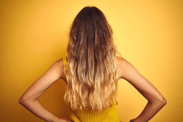 Obraz premium Young beautiful woman wearing t-shirt over yellow isolated background standing backwards looking away with arms on body