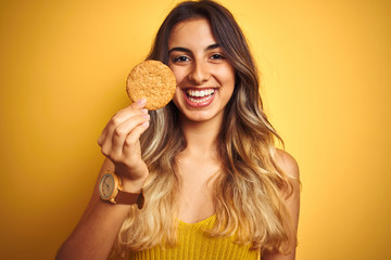 Young beautiful woman eating biscuit over grey isolated background with a happy face standing and...
