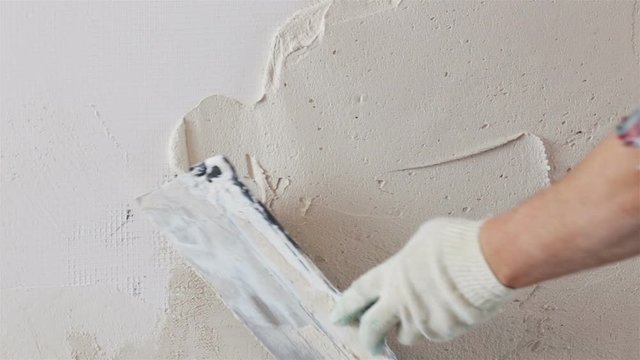 Construction worker with long trowel plastering a wall
