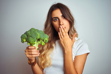 Young beautiful woman eating broccoli over grey isolated background cover mouth with hand shocked with shame for mistake, expression of fear, scared in silence, secret concept