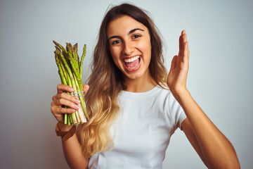 Young beautiful woman eating asparagus over grey isolated background very happy and excited, winner expression celebrating victory screaming with big smile and raised hands