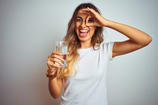 Young Beautiful Woman Drinking A Glass Of Water Over White Isolated Background With Happy Face Smiling Doing Ok Sign With Hand On Eye Looking Through Fingers