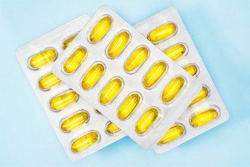 Omega 3 capsules package in three blisters. Top view fish oil capsules, closeup on light blue background.