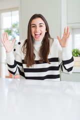 Beautiful young woman wearing stripes sweater celebrating crazy and amazed for success with arms raised and open eyes screaming excited. Winner concept