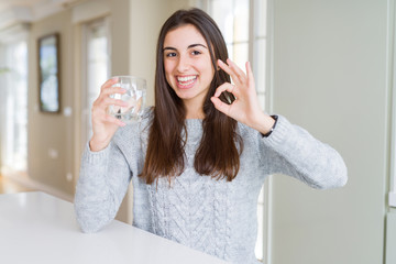 Beautiful young woman drinking a fresh glass of water doing ok sign with fingers, excellent symbol