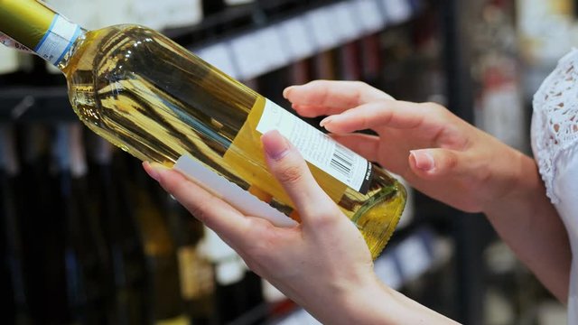 Woman chooses wine in the Supermarket, customer selects product, reads the composition on the bottle, holds the wine in hand in the store in close-up