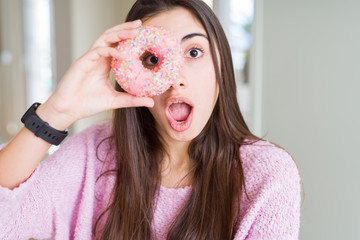 Beautiful young woman eating pink chocolate chips donut scared in shock with a surprise face, afraid and excited with fear expression