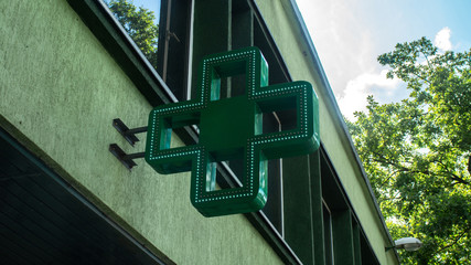 Pharmacy green cross sign with led light on the wall exterior single object sunny weather