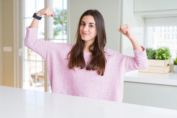 Beautiful young woman wearing pink sweater showing arms muscles smiling proud. Fitness concept.