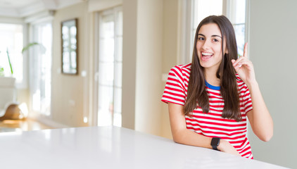 Beautiful young woman wearing casual stripes t-shirt pointing finger up with successful idea. Exited and happy. Number one.