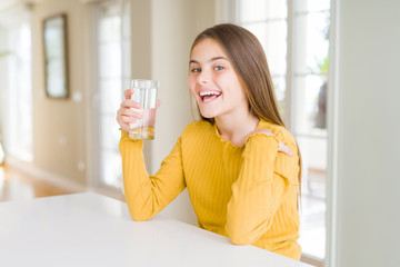 Beautiful young girl kid drinking a fresh glass of water with surprise face pointing finger to himself