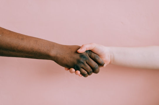 Handshake between african and caucasian male and female over pink background