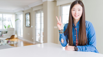 Young beautiful asian woman with long hair wearing denim jacket showing and pointing up with fingers number two while smiling confident and happy.