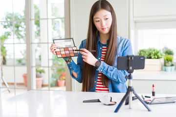 Beautiful Asian influencer woman recording make up tutorial using smartphone camera with a...