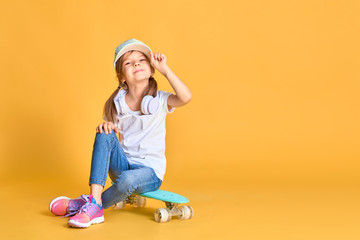 Stylish little girl child girl in casual with skateboard over yellow background. © zamuruev
