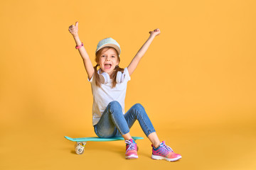 Stylish little girl child girl in casual with skateboard over yellow background.