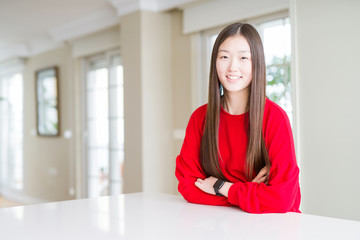 Beautiful Asian woman wearing red sweater on white table happy face smiling with crossed arms looking at the camera. Positive person.