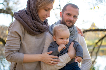 Fototapeta premium Happy family couple with their little child in autumn park in sunny day.
