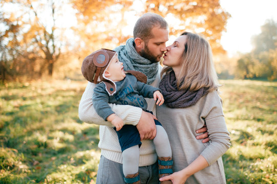 Stylish family couple hug funny child in pilot helmet and kissing in autumn park