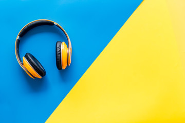Wireless headphones as gadgets for listen to the music on yellow and blue background top view mock...