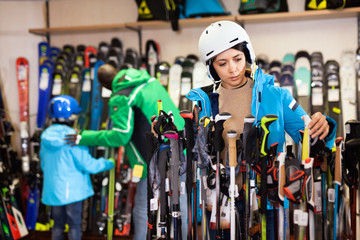 Attractive girl choosing ski poles for skiing in store of sports equipment