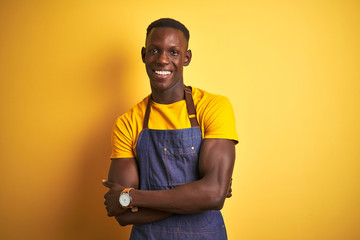 African american bartender man wearing apron standing over isolated yellow background happy face...