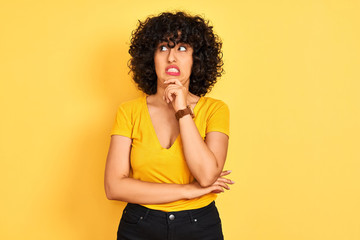 Young arab woman with curly hair wearing t-shirt standing over isolated yellow background Thinking worried about a question, concerned and nervous with hand on chin
