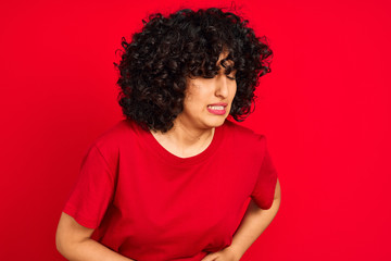Fototapeta na wymiar Young arab woman with curly hair wearing casual t-shirt over isolated red background with hand on stomach because indigestion, painful illness feeling unwell. Ache concept.