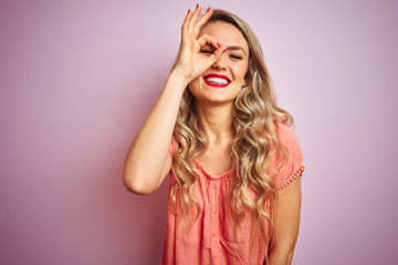 Young beautiful woman wearing t-shirt standing over pink isolated background doing ok gesture with hand smiling, eye looking through fingers with happy face.