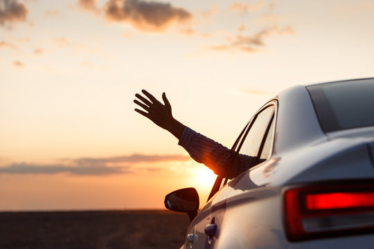 Man inside car showing his hand outdoor/leaning out of car window at sunset, relaxing, enjoying road trip and feeling the air and freedom. 